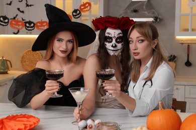 Group of women in scary costumes with cocktails celebrating Halloween indoors