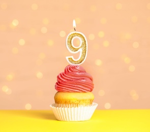 Photo of Birthday cupcake with number nine candle on table against festive lights