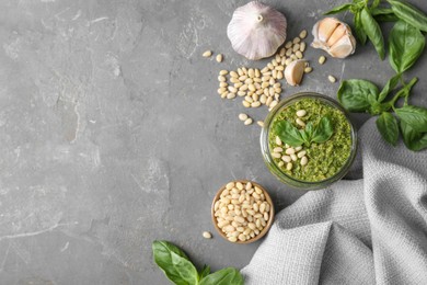 Photo of Jar of delicious pesto sauce and ingredients on grey table, flat lay. Space for text