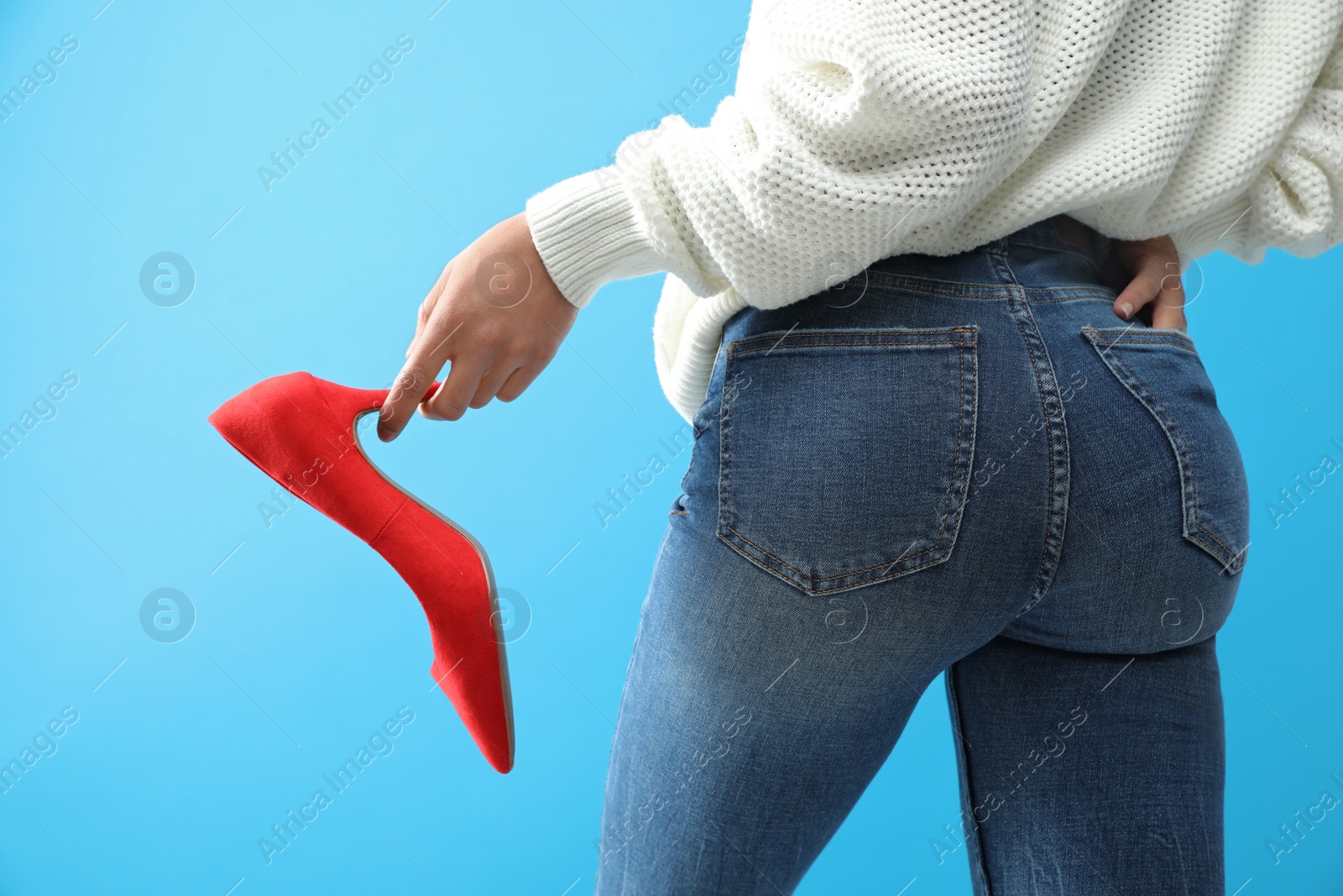 Photo of Woman in jeans holding red shoe on blue background, closeup