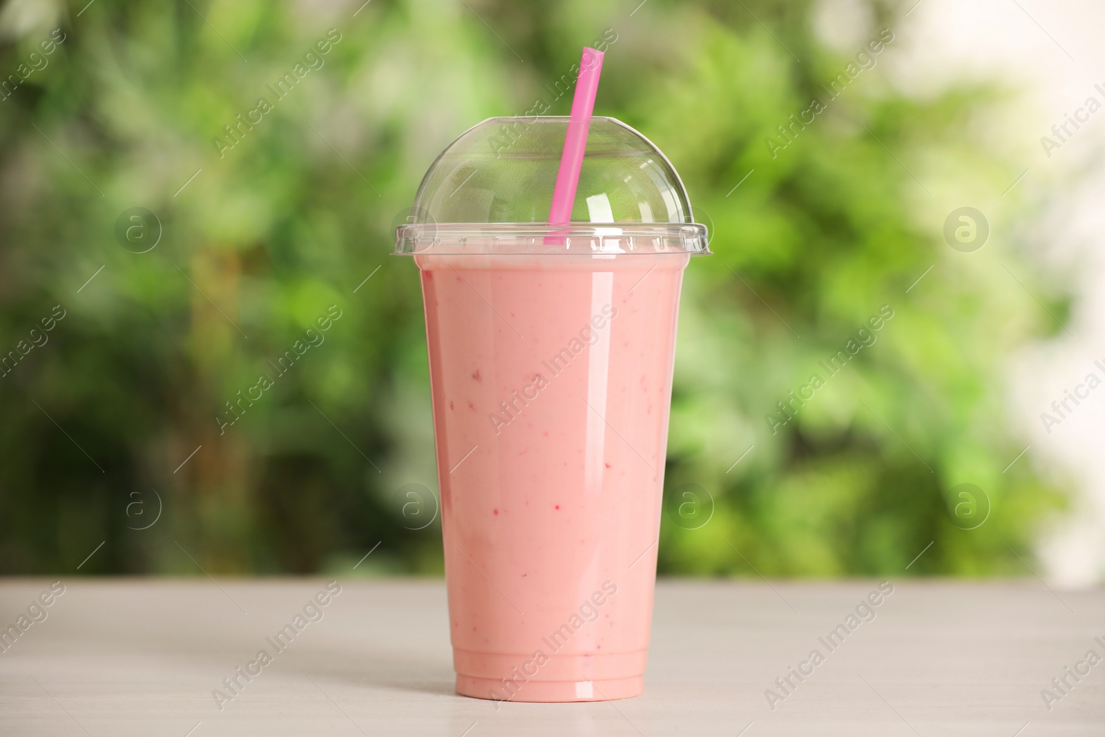 Photo of Plastic cup of tasty smoothie on wooden table outdoors