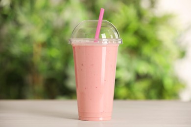 Photo of Plastic cup of tasty smoothie on wooden table outdoors