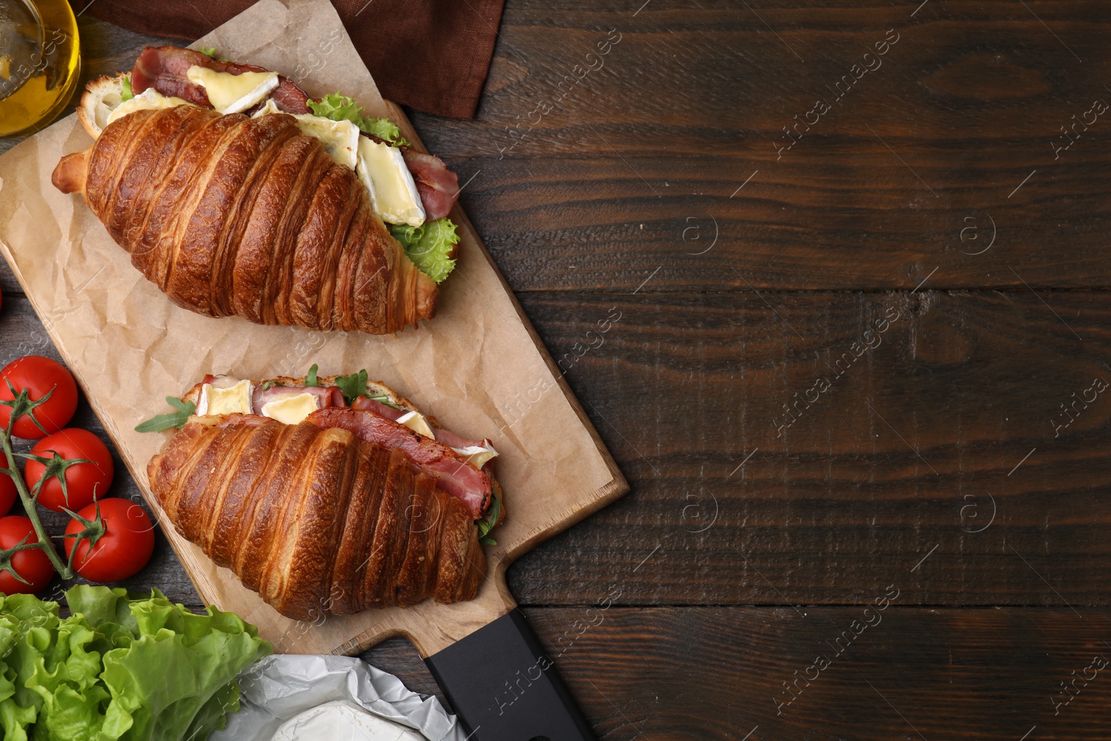 Photo of Tasty croissants with brie cheese, ham and bacon on wooden table, flat lay. Space for text