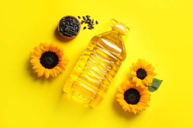 Bottle of cooking oil, sunflowers and seeds on yellow background, flat lay