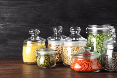 Different types of legumes and cereals in glass jars on wooden table. Organic grains