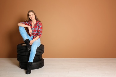 Young woman in seductive outfit with car tires on color wall background