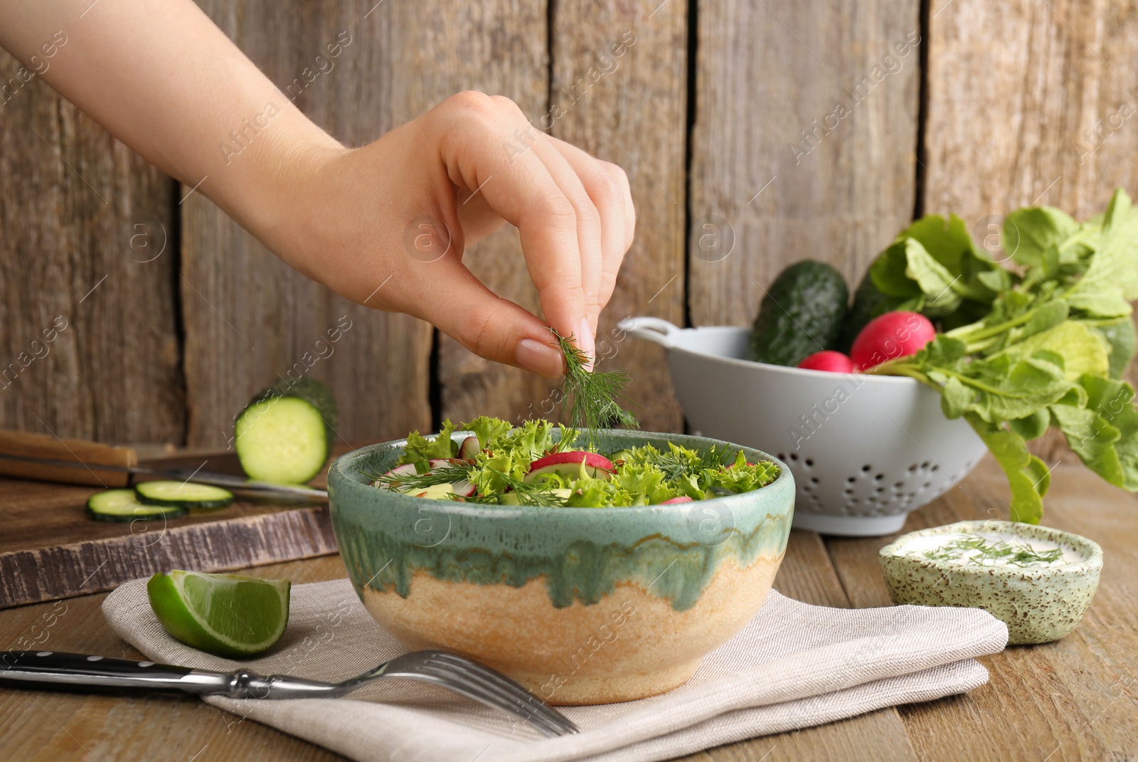 Photo of Woman adding dill into radish salad at wooden table, closeup