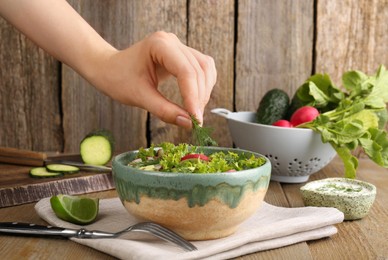 Woman adding dill into radish salad at wooden table, closeup