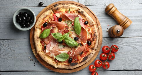 Photo of Tasty pizza with cured ham, olives, tomatoes and basil on gray wooden table, flat lay