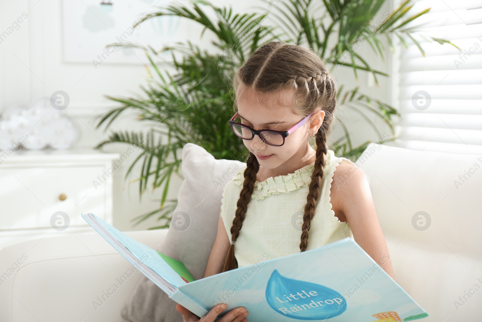 Photo of Cute little girl reading book on sofa at home