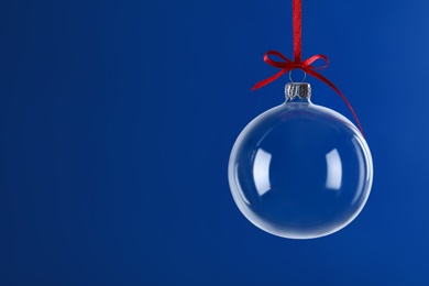 Photo of Transparent glass Christmas ball with red ribbon and bow against blue background. Space for text