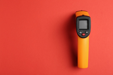 Photo of Modern non-contact infrared thermometer on red background, top view. Space for text