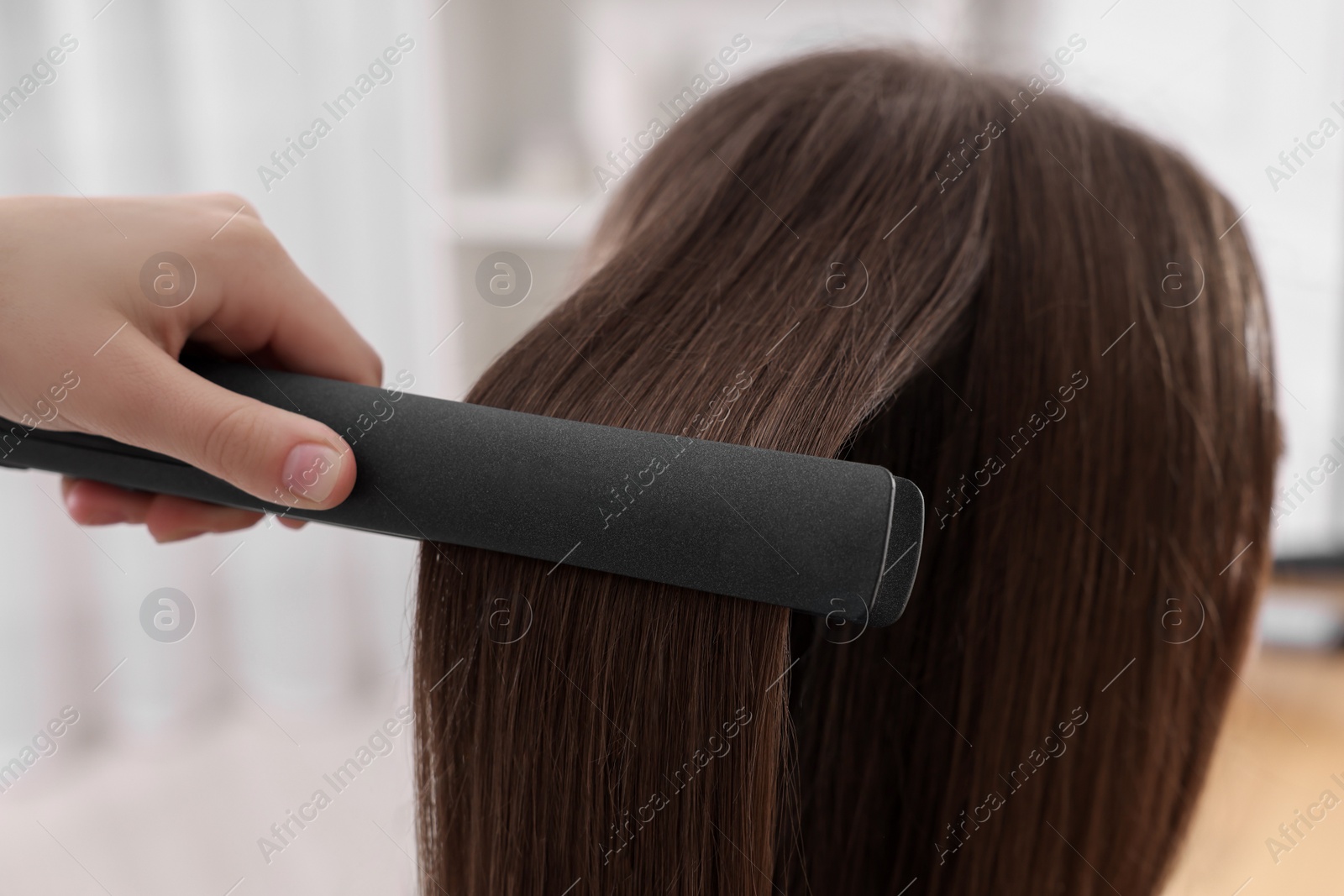 Photo of Hairdresser straightening woman's hair with flat iron indoors, closeup