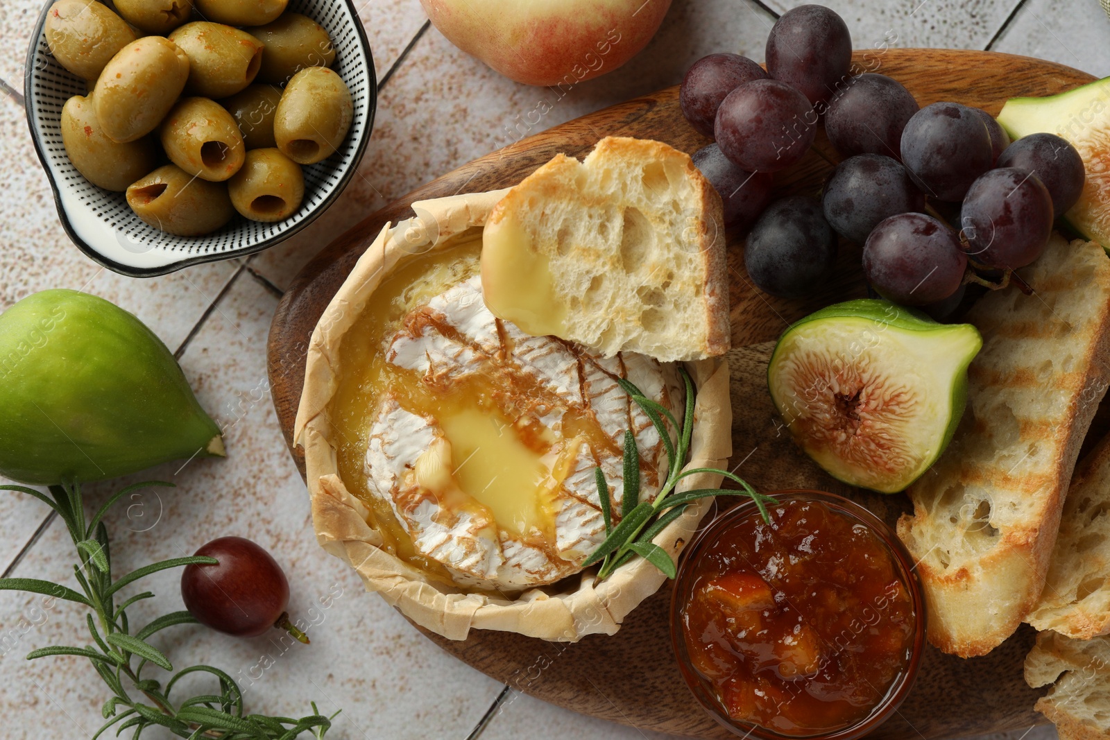 Photo of Tasty baked brie cheese and products on light tiled table, flat lay