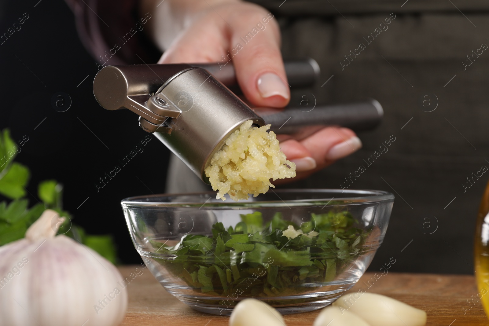 Photo of Woman squeezing garlic with press at wooden table, closeup