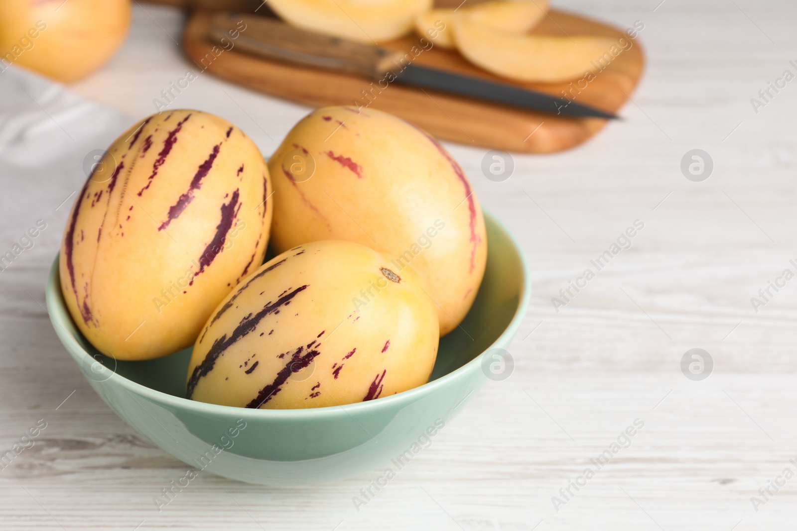 Photo of Fresh ripe pepino melons in bowl on white wooden table. Space for text