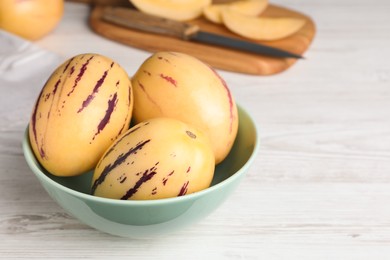 Photo of Fresh ripe pepino melons in bowl on white wooden table. Space for text