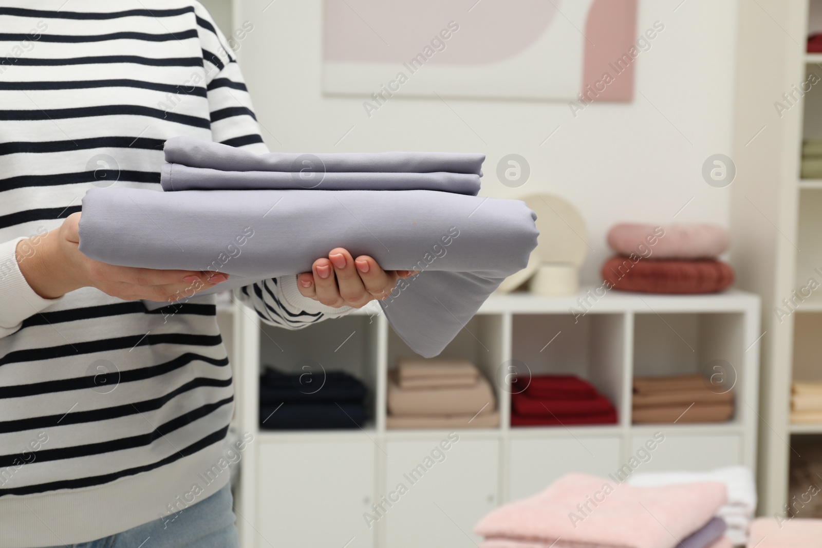 Photo of Woman holding stack of bed linens in home textiles store, closeup. Space for text