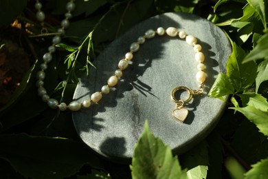 Photo of Stylish presentation of elegant pearl necklace on stone stand outdoors