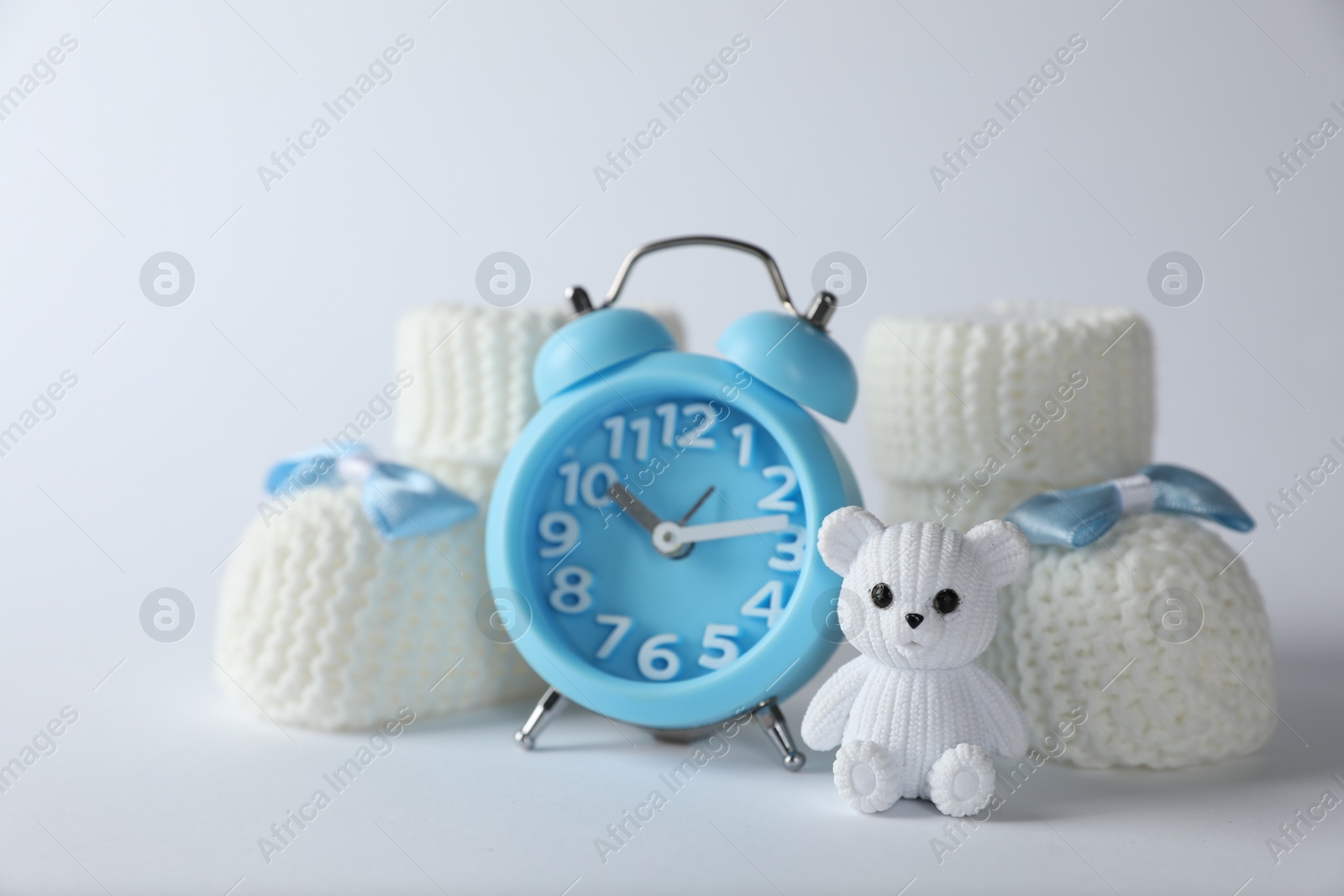 Photo of Alarm clock, toy bear and baby booties on white background. Time to give birth