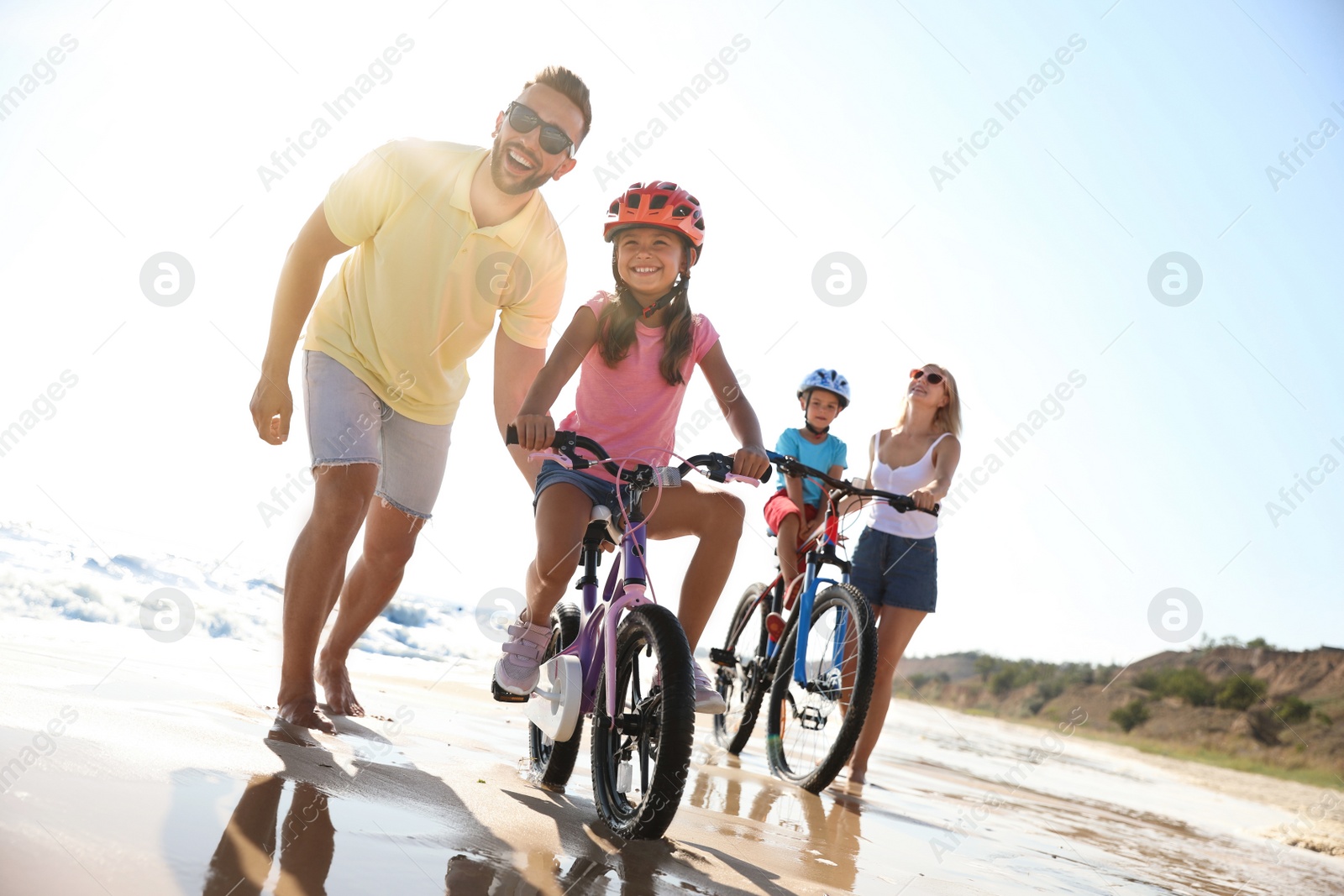 Photo of Happy parents teaching children to ride bicycles on sandy beach near sea