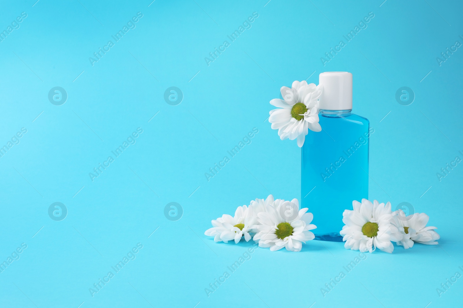 Photo of Fresh mouthwash in bottle and flowers on light blue background. Space for text