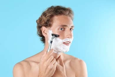 Handsome young man shaving on color background