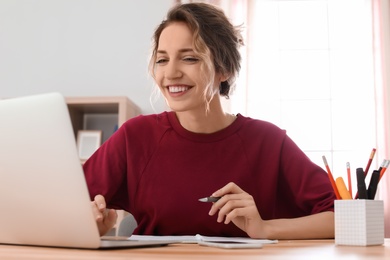 Photo of Young woman working with laptop at desk. Home office