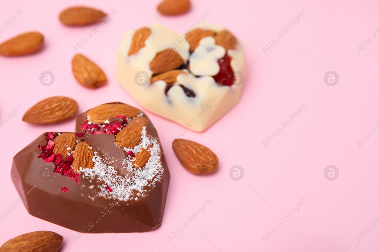 Photo of Tasty chocolate heart shaped candies with nuts on pink background, closeup. Space for text