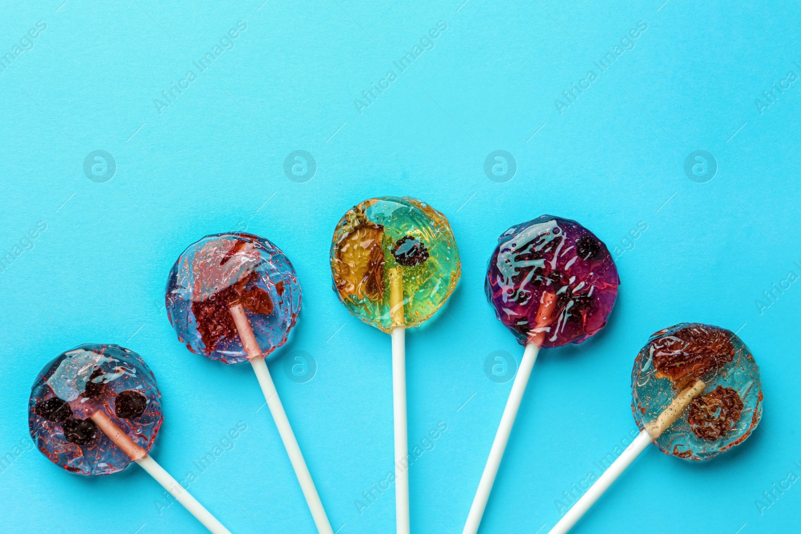 Photo of Sweet colorful lollipops with berries on light blue background, flat lay