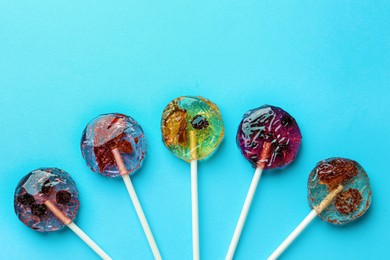 Sweet colorful lollipops with berries on light blue background, flat lay