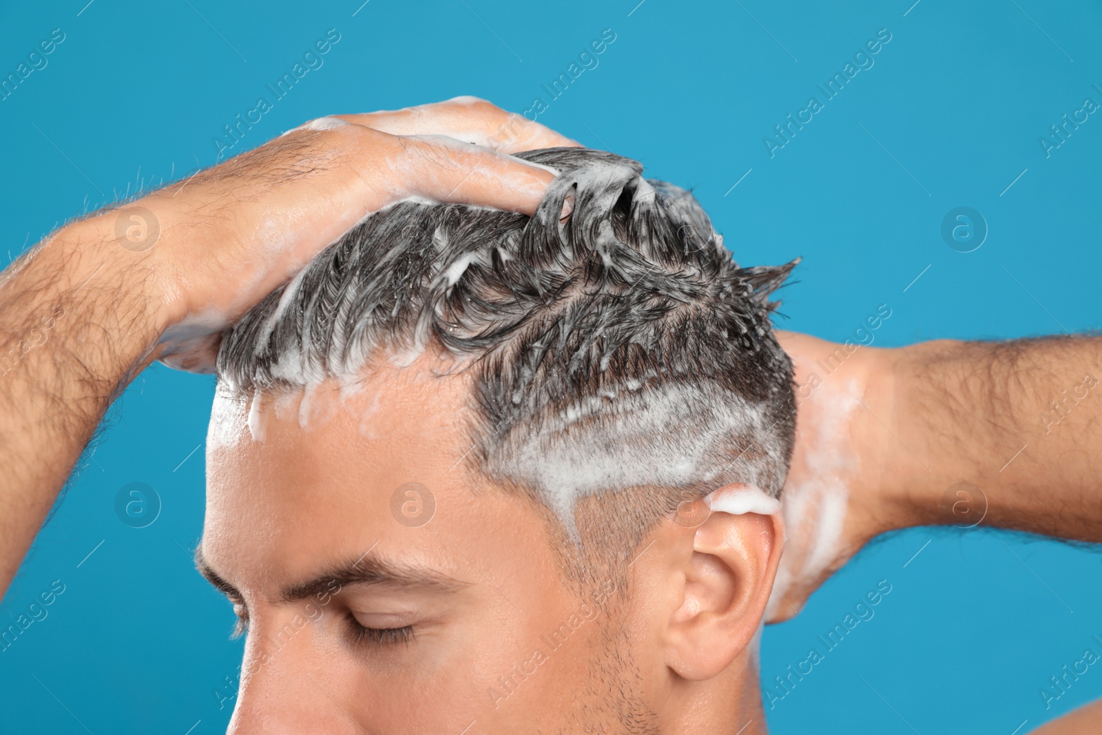 Photo of Handsome man washing hair on light blue background, closeup