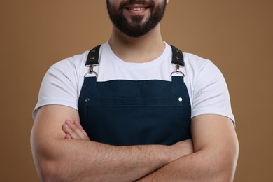 Photo of Smiling man in kitchen apron with crossed arms on brown background, closeup. Mockup for design