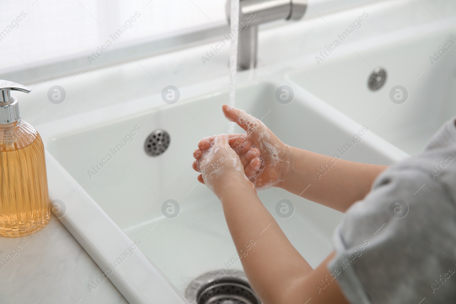 Photo of Little girl washing hands with liquid soap at home, closeup