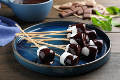 Delicious marshmallows covered with chocolate on wooden table