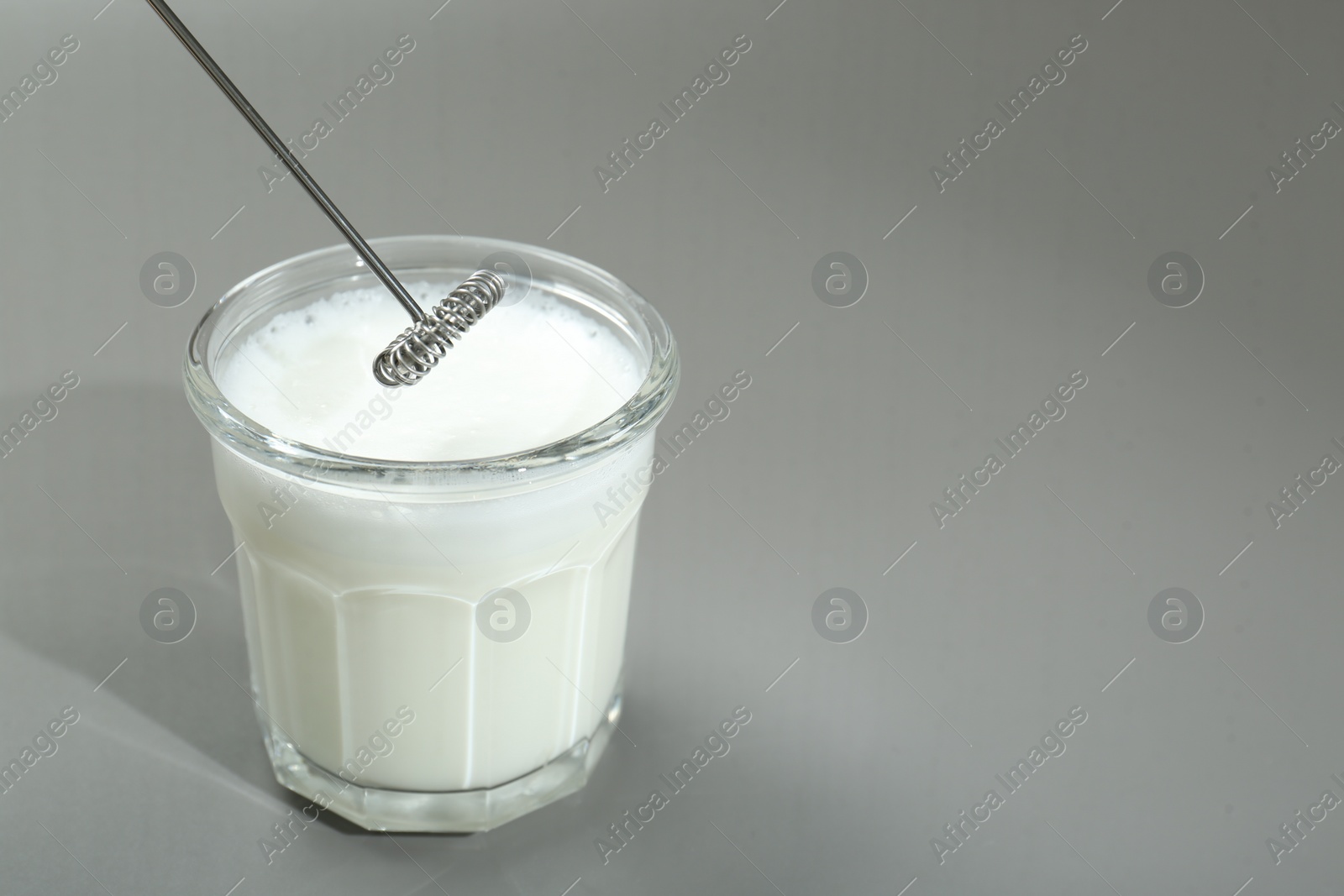 Photo of Mini mixer (milk frother) and whipped milk in glass on grey background. Space for text