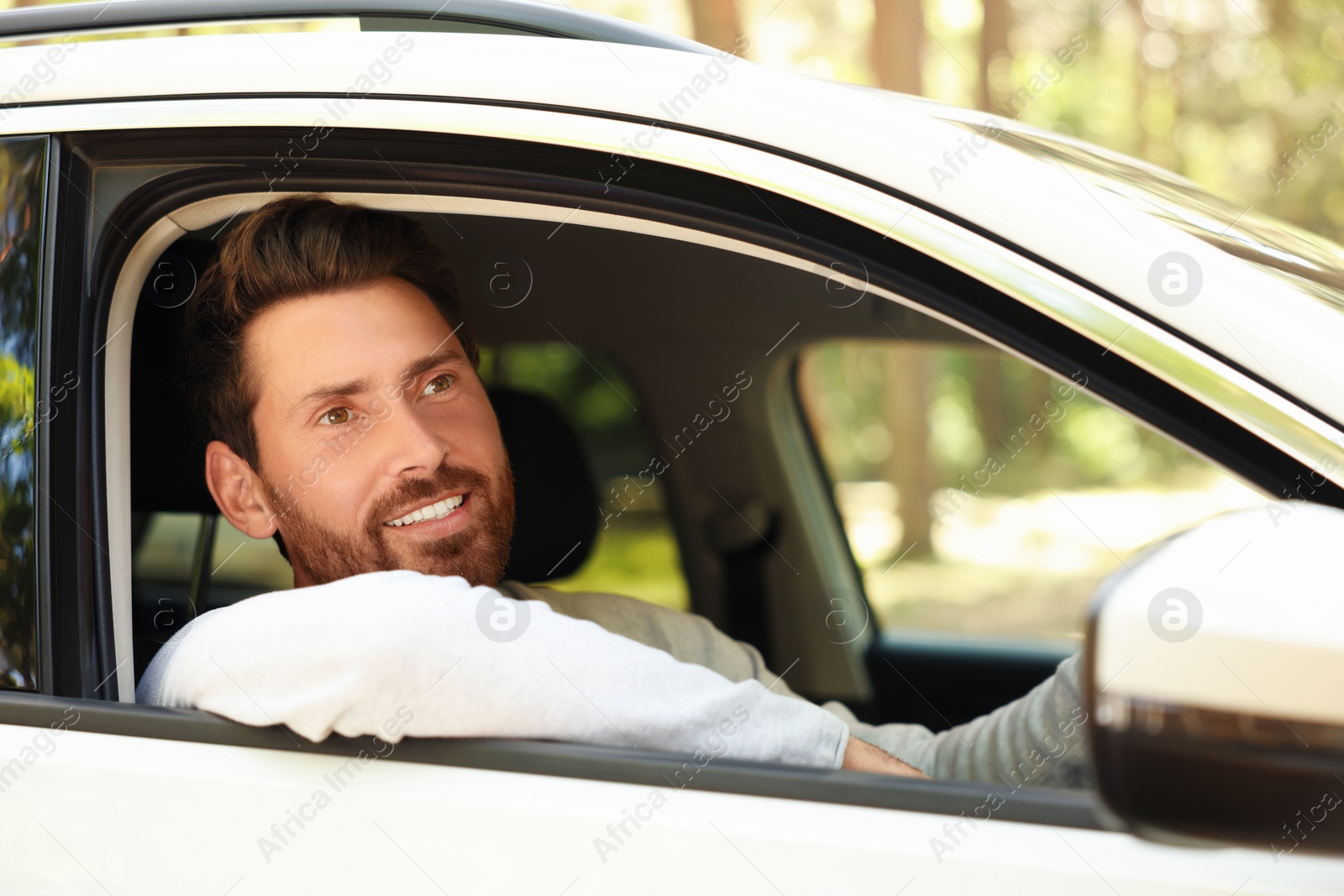Photo of Happy bearded man looking out of car window, view from outside. Enjoying trip