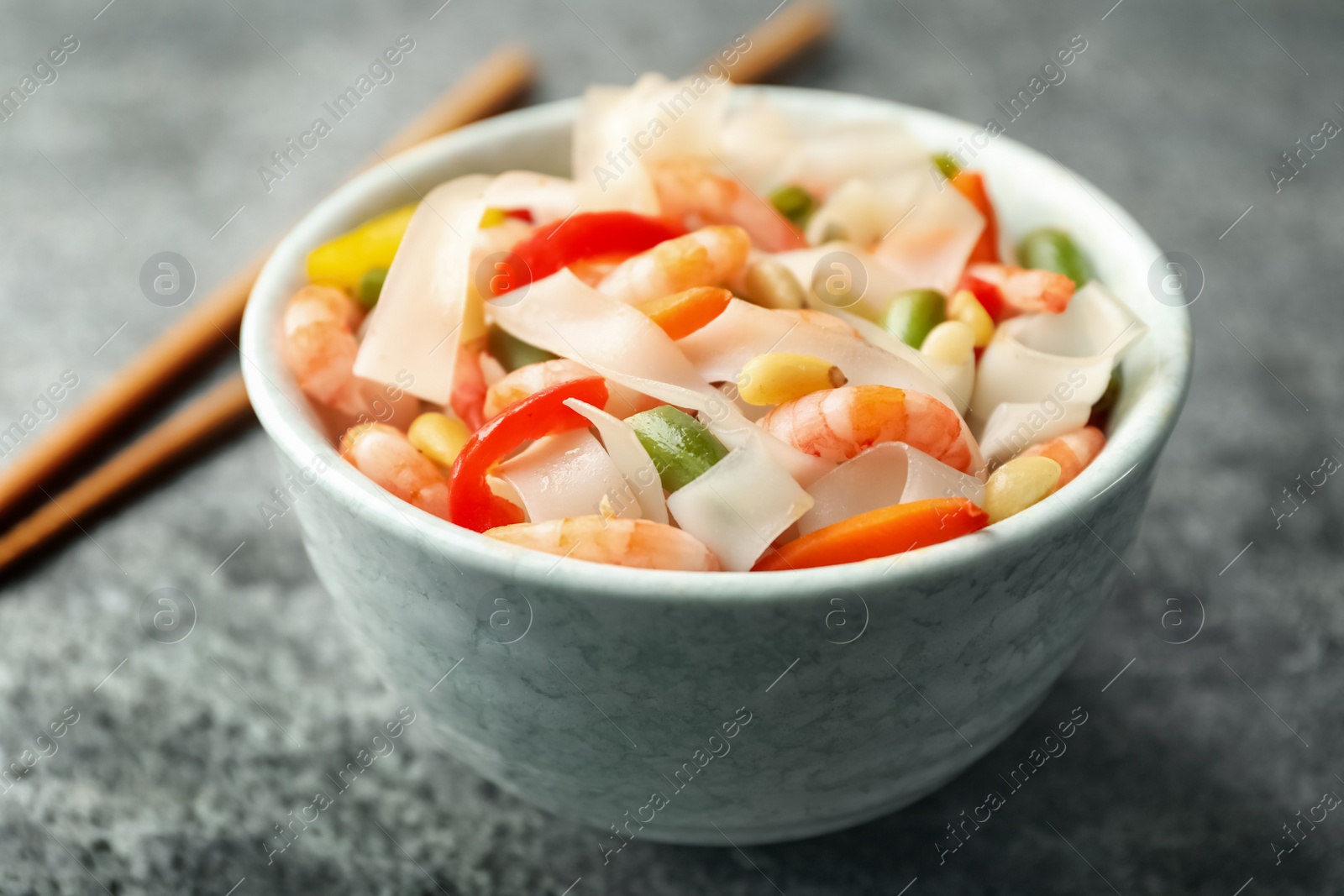 Photo of Tasty cooked rice noodles with shrimps and vegetables on grey table