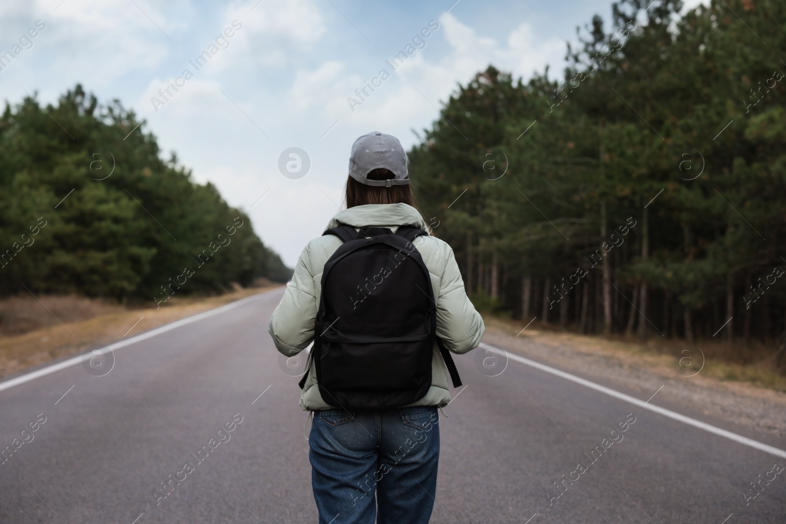 Photo of Woman with backpack on road near forest, back view