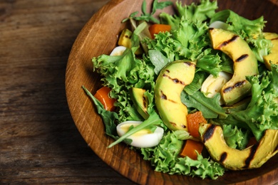 Photo of Delicious avocado salad with boiled eggs in bowl on wooden table, closeup