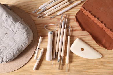 Clay and set of modeling tools on wooden table, flat lay