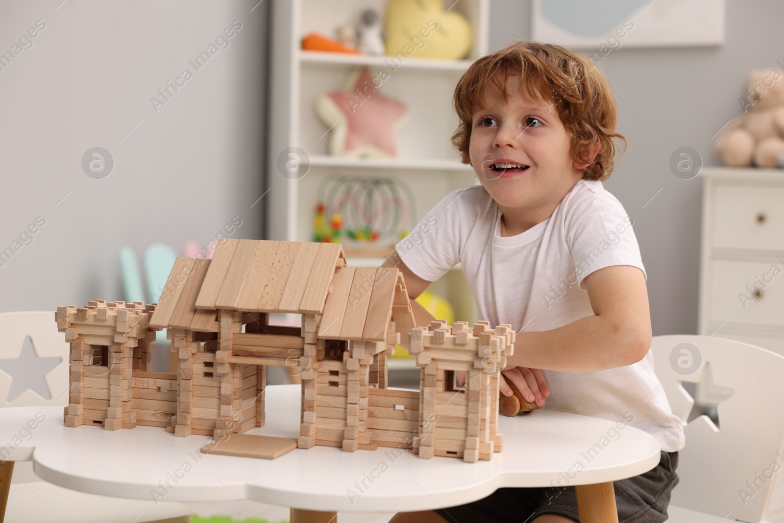 Photo of Little boy playing with wooden entry gate at white table in room. Child's toy