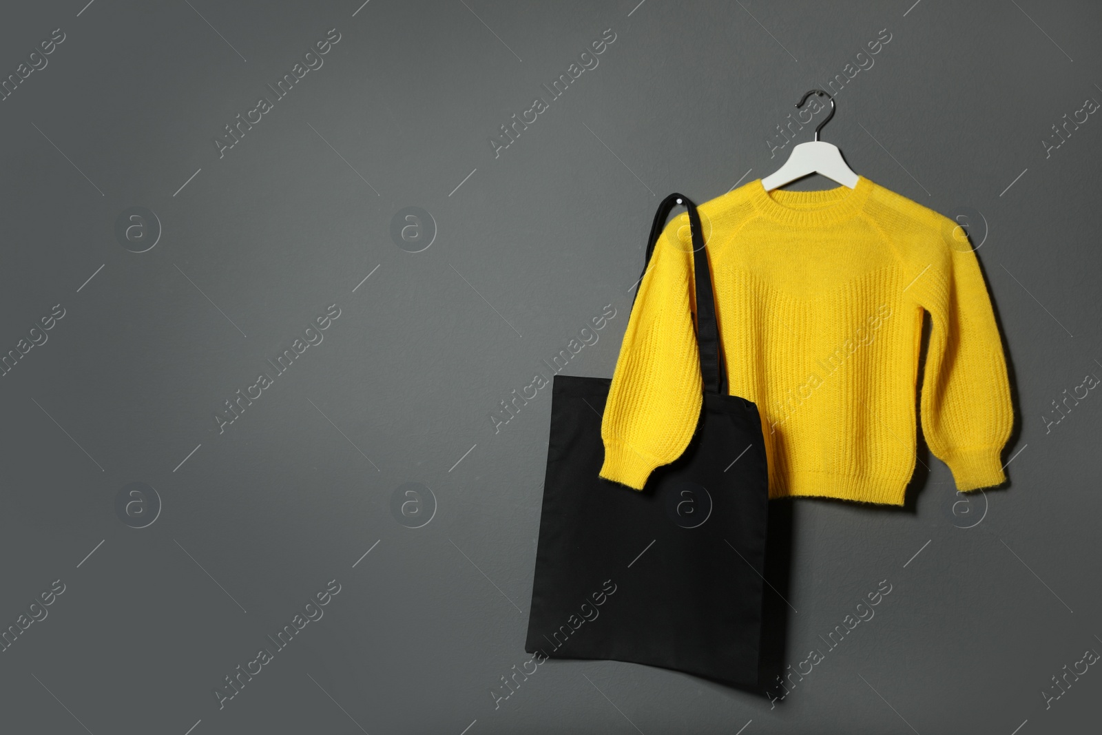 Photo of Eco tote bag and sweater hanging on grey wall. Space for text