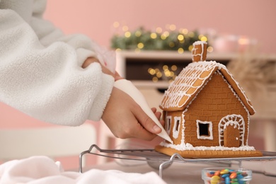 Woman decorating gingerbread house with icing at table, closeup