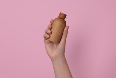 Woman holding bottle of cosmetic product on pink background, closeup