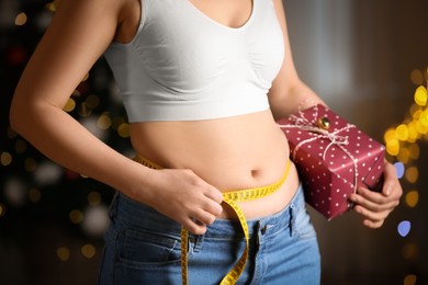 Photo of Woman with gift box and measuring tape indoors, closeup. Overweight problem after New Year party