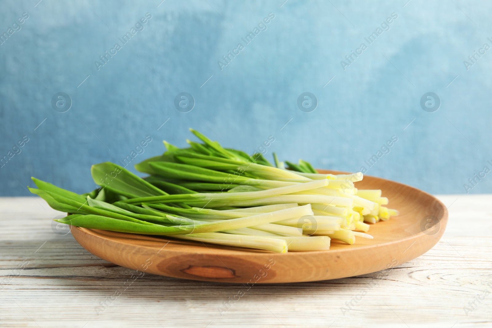 Photo of Wooden plate with wild garlic or ramson on table against color background. Space for text