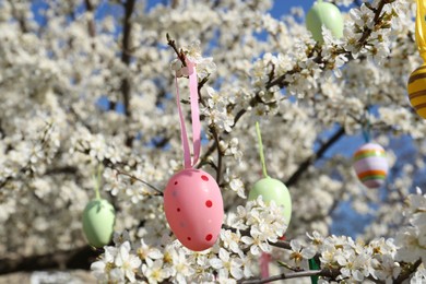 Photo of Beautifully painted Easter eggs hanging on blooming cherry tree outdoors