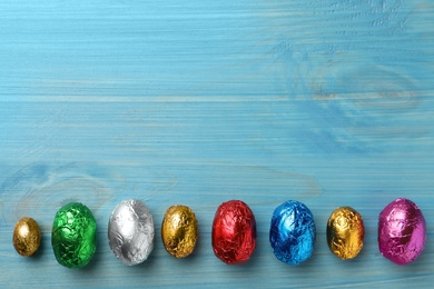 Chocolate eggs wrapped in colorful foil on light blue wooden table, flat lay. Space for text