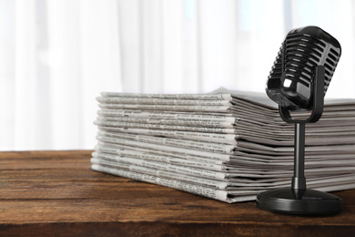 Photo of Newspapers and vintage microphone on wooden table. Journalist's work